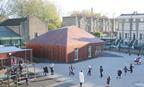 The building sits in the corner of the playground like a toy house, wrapped with cedar floorboards.