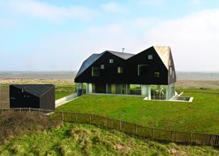 The faceted roof floats above a glazed ground floor, partially sunk into the surrounding dunes..